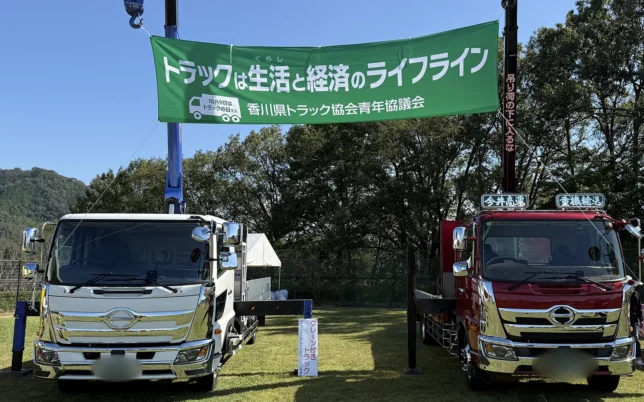 クレーンを伸ばしたトラック2台と、香川県トラック協会青年協議会の「トラックは生活と経済のライフライン」の横断幕