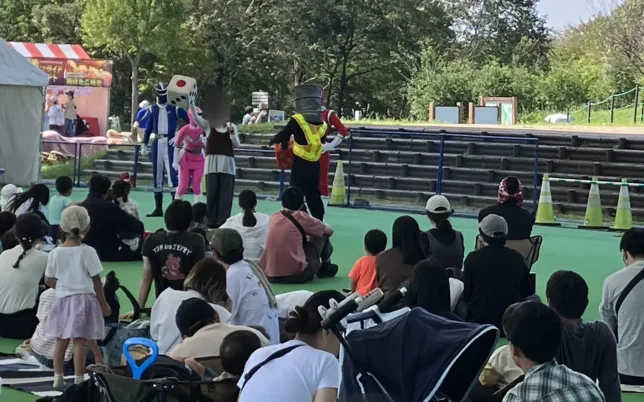 ドームの下のステージで行われたトラックレンジャーショーと、座って見る親子連れ